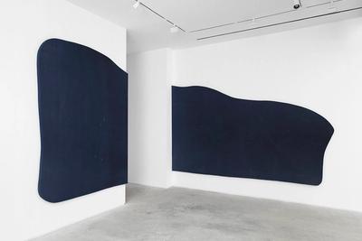Two large, dark blue abstract shapes mounted on white walls in a minimalist gallery.