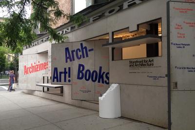 The image depicts a storefront at 97 Kenmare Street, New York, NY, with concrete panels attached to its exterior, advertising various art and architecture programs and exhibitions. Prominent text includes "Archizines" in red, "Arch-Art! Books" in purple, and "Storefront for Art and Architecture" in black along with gallery hours and address details. A white cylindrical sculpture sits near the entrance. A brick building, tree branches, and a person with a bag and shawl are visible nearby.