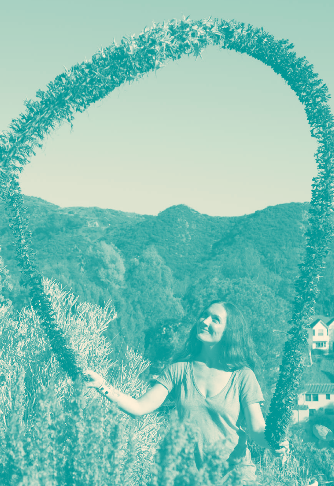 A person forms a circular wreath with arms, standing against soft green-toned hills and trees in an ethereal outdoor setting, evoking a dreamy, organic atmosphere through warm lighting and vintage filters.