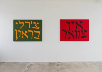 Artworks on white wall: left dark green with yellow Hebrew script in two lines, right red with black Hebrew script in two lines, concrete floor.