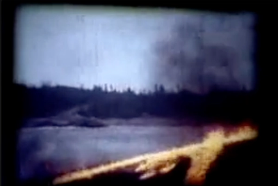 Fire burns along a shoreline with a dark forest and smoky sky.