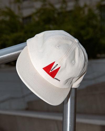 White baseball cap with red and black "Brooklyn Usetum" logo on front, resting on metal railing outdoors.