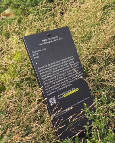 Plaque for Mark Di Suvero (1933–2022), Shanghai-born steel artist. White text on black: dynamic sculptures in parks/streets. QR code 'BROOKLYN ICON.' Brooklyn Museum's 200th Anniversary.
