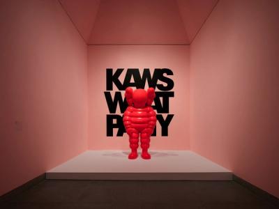 Red KAWS Companion figure stands before black text on a pink wall.