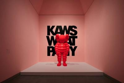 Red KAWS Companion figure stands before black text on a pink wall.