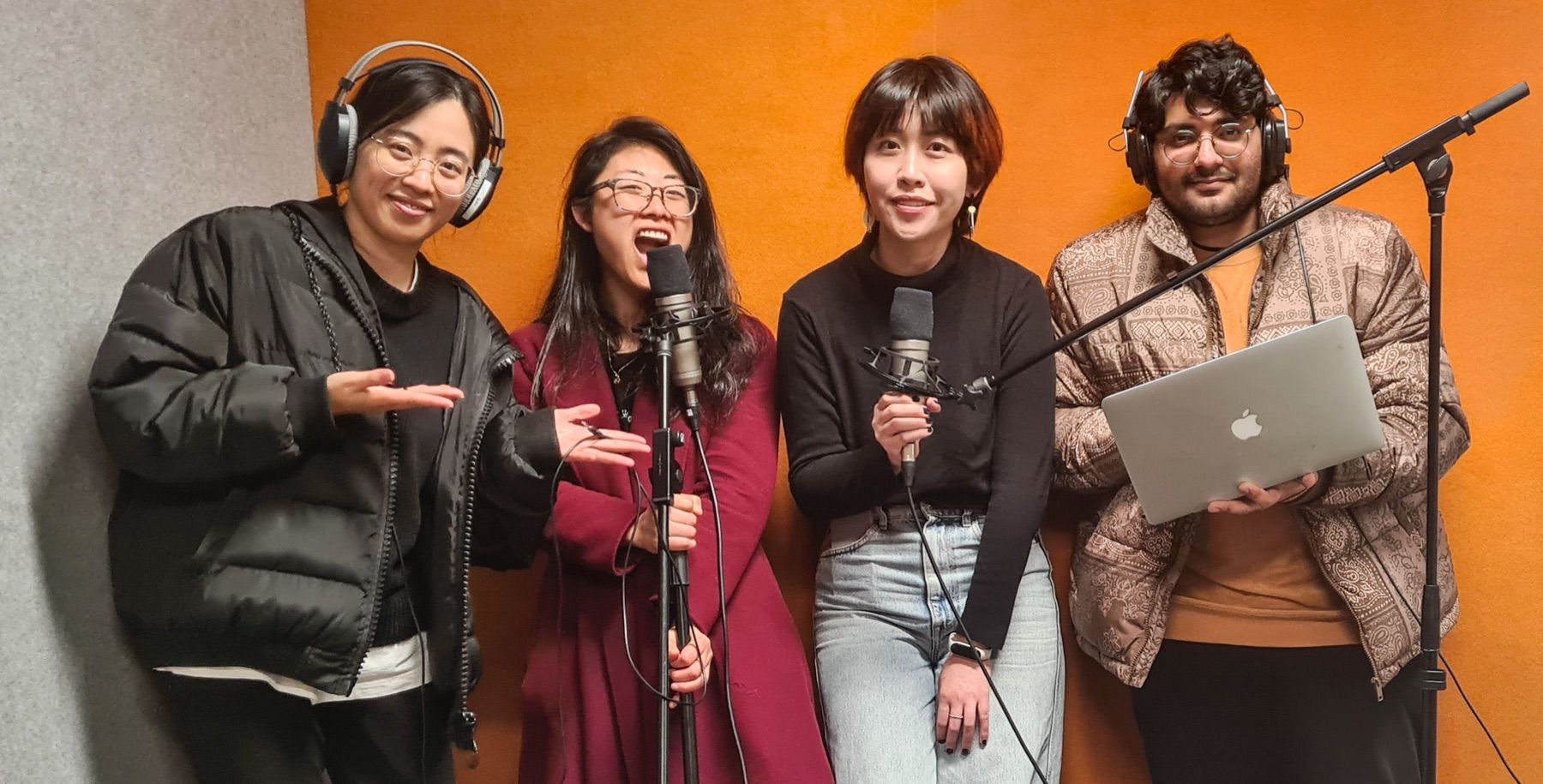 Four people laughing at microphones during a Voices of Us podcast recording