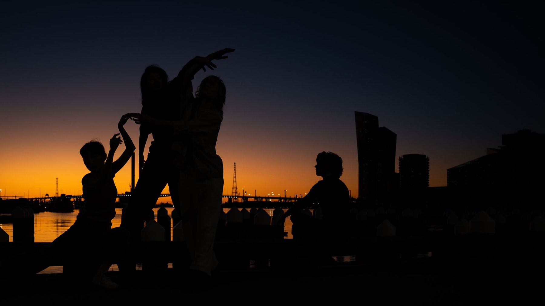 Dancers in silhouette against a sunset over the water