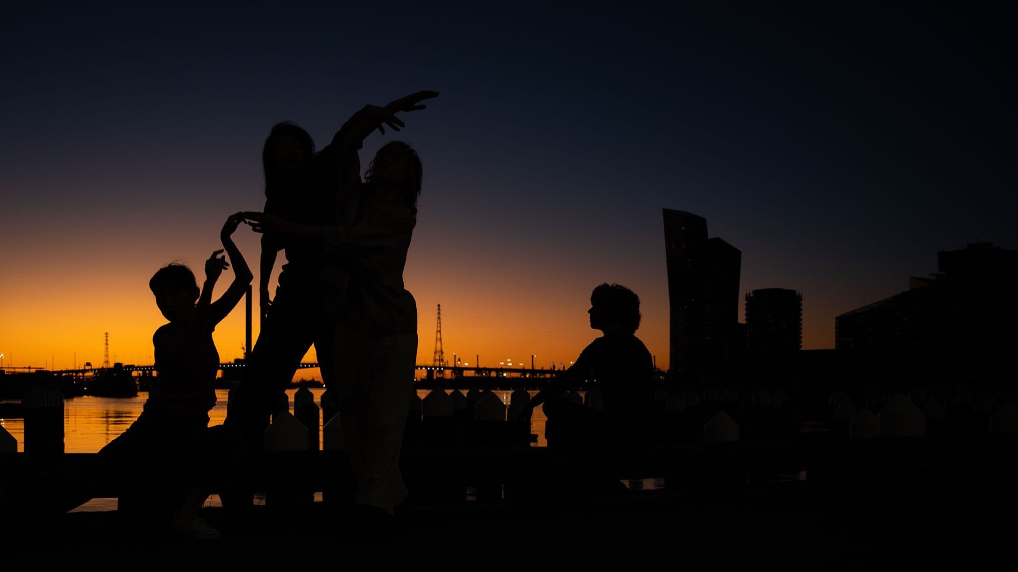 Dancers in silhouette against a sunset over the water