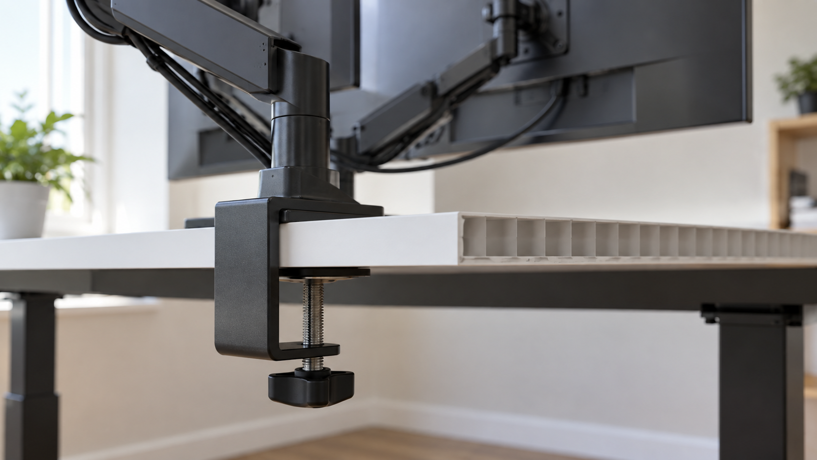 Close-up of a dual monitor arm clamp gripping the back edge of a thin white hollow-board tabletop, with two monitors on the arm above it.