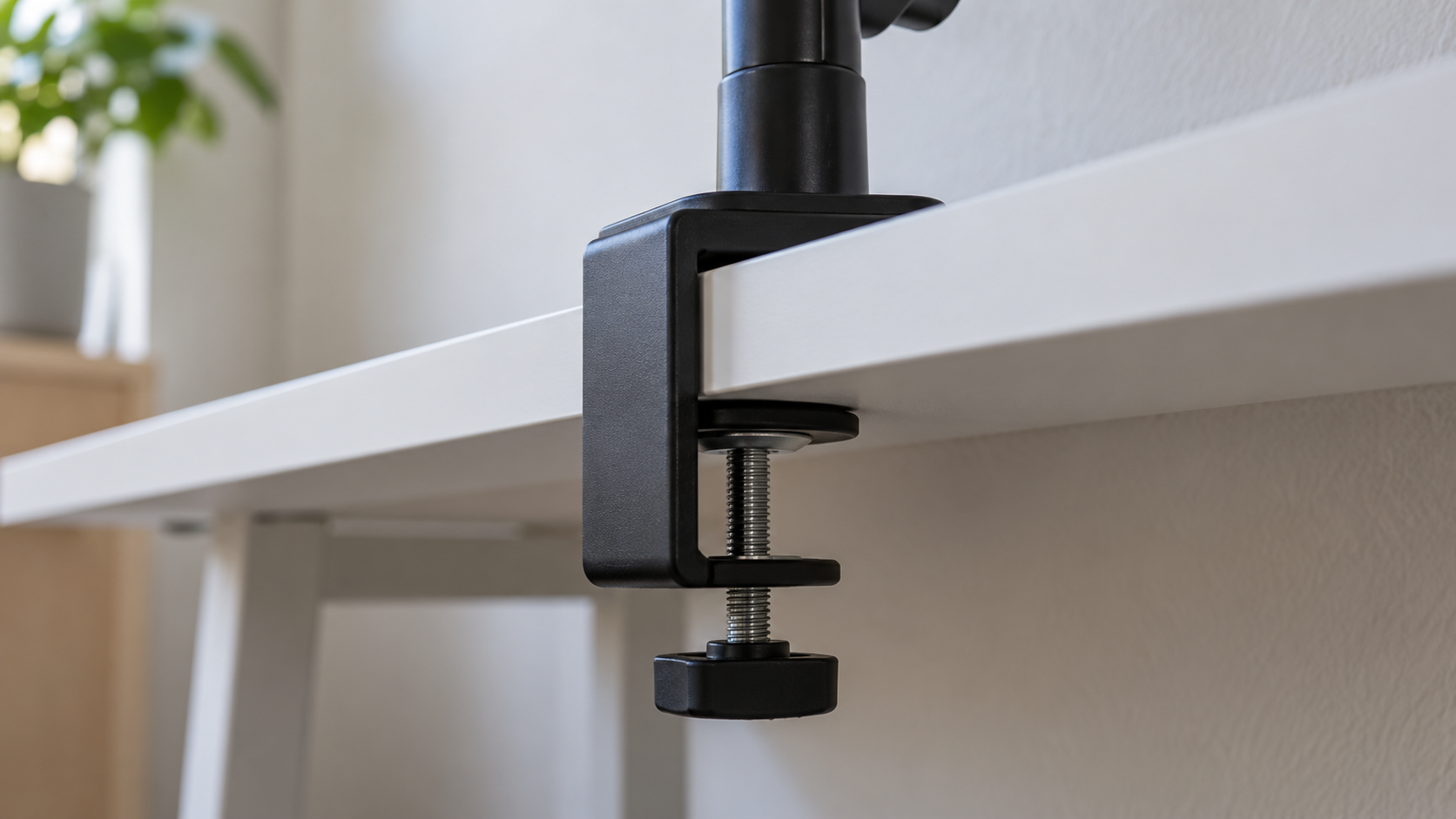 Close-up of a monitor arm C-clamp gripping the rear edge of a thin white flat-pack tabletop.