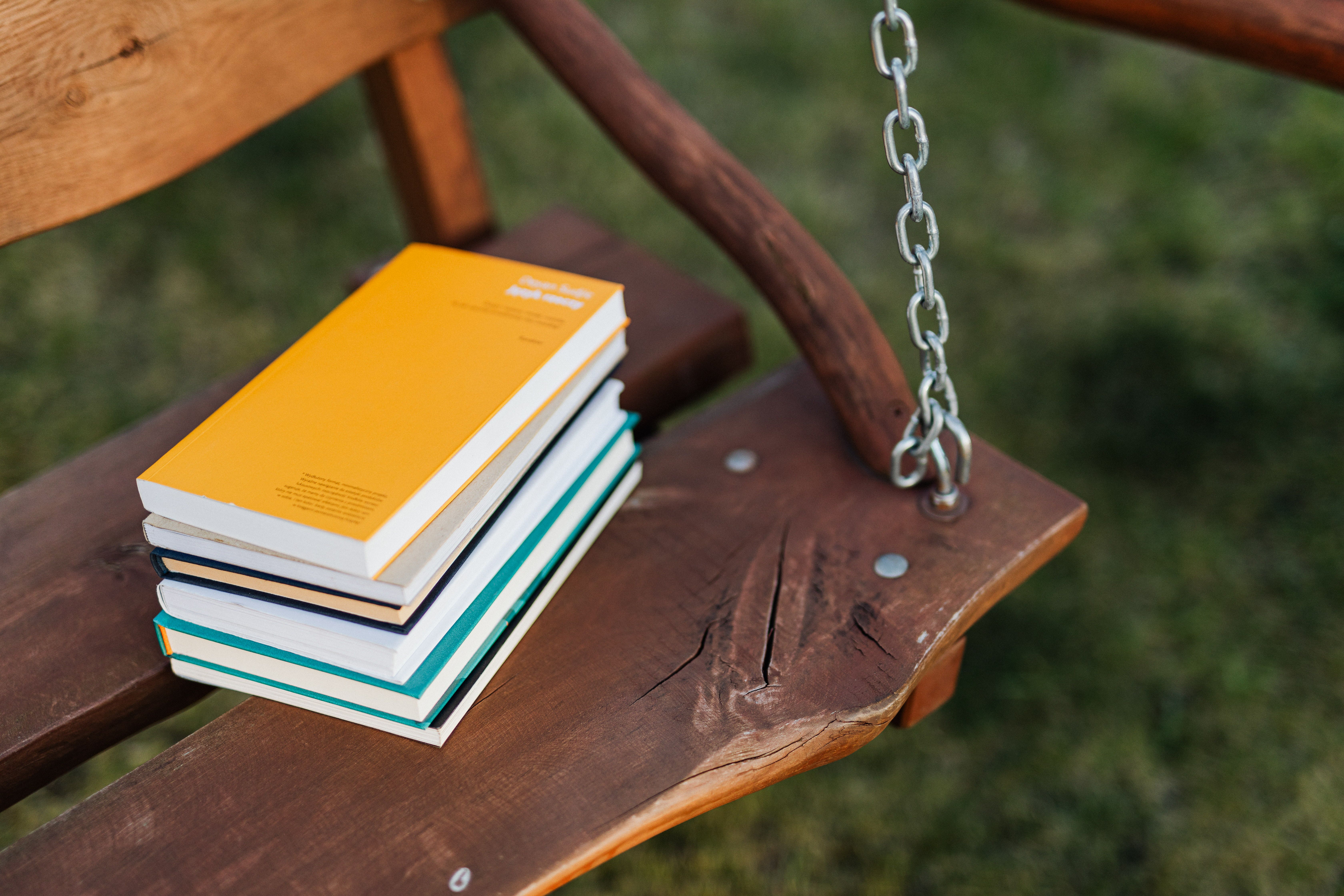 A stack of books sits on an outdoor wooden swing