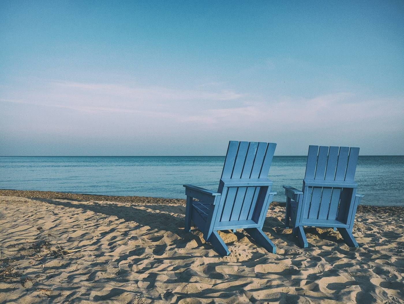 two deck chairs on sand overlooking ocean