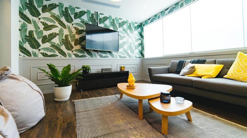 living room with palm print wallpaper, couch, coffee table and tv on wall
