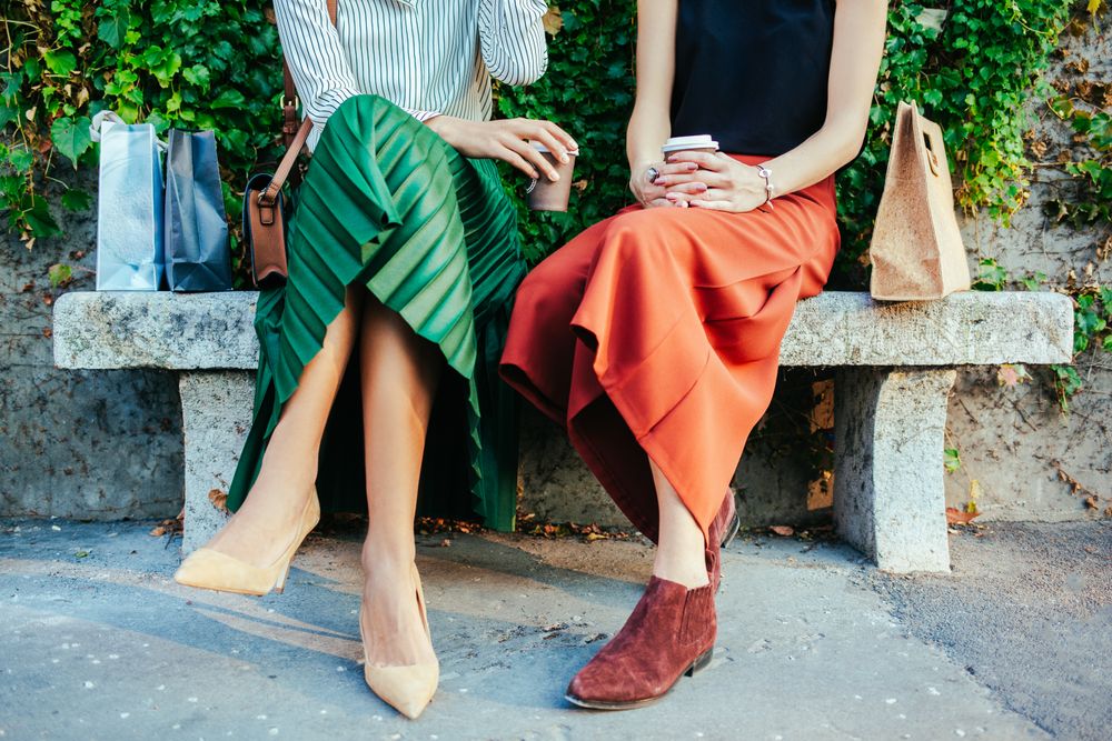 Two women sitting on park bench, drinking coffee 