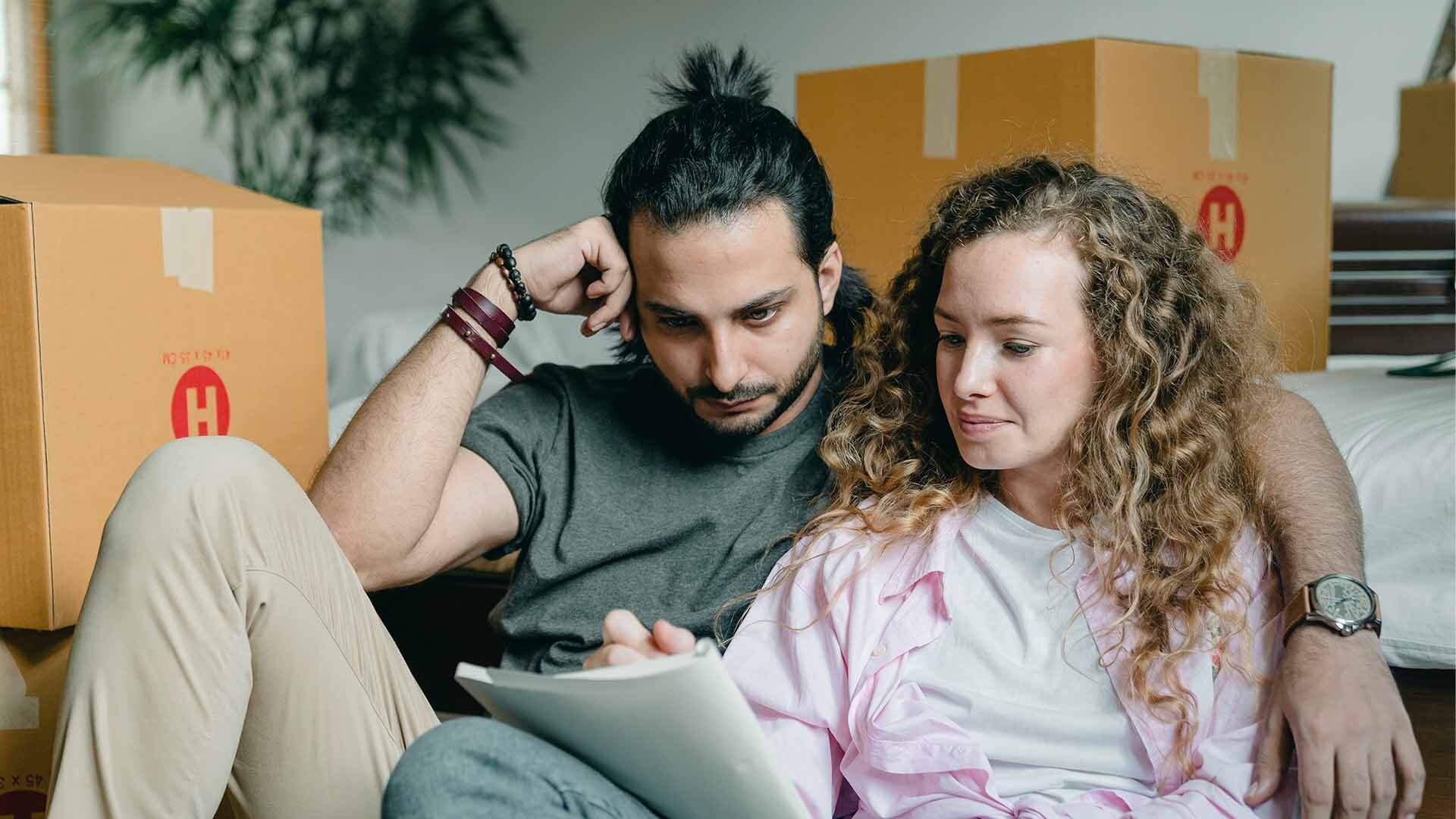 Couple sitting on couch surrounded by boxes and looking at note pad