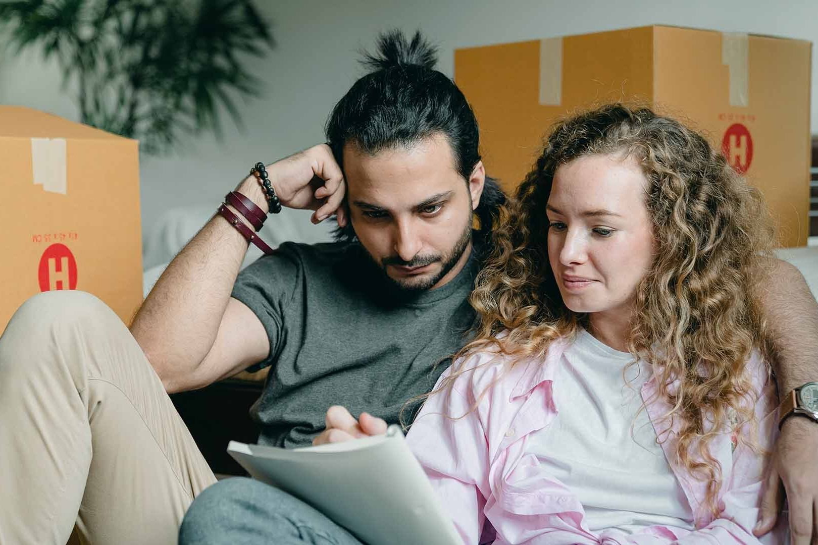 Couple sitting on couch surrounded by boxes and looking at note pad