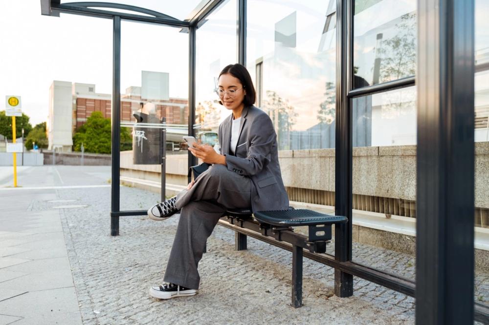 Woman sits at a bus stop and uses a smartphone