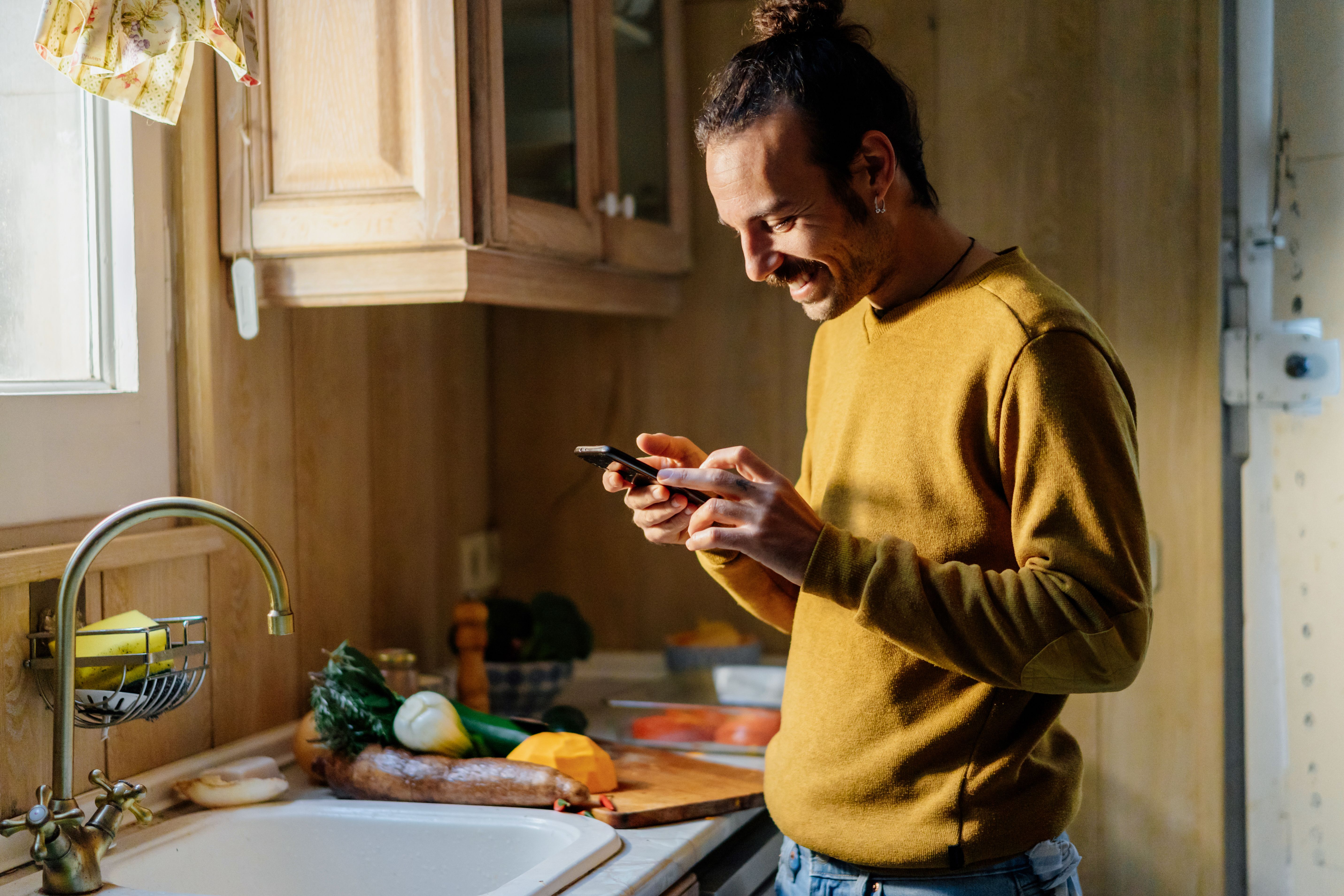 Man standing in kitchen, smiling at his phone
