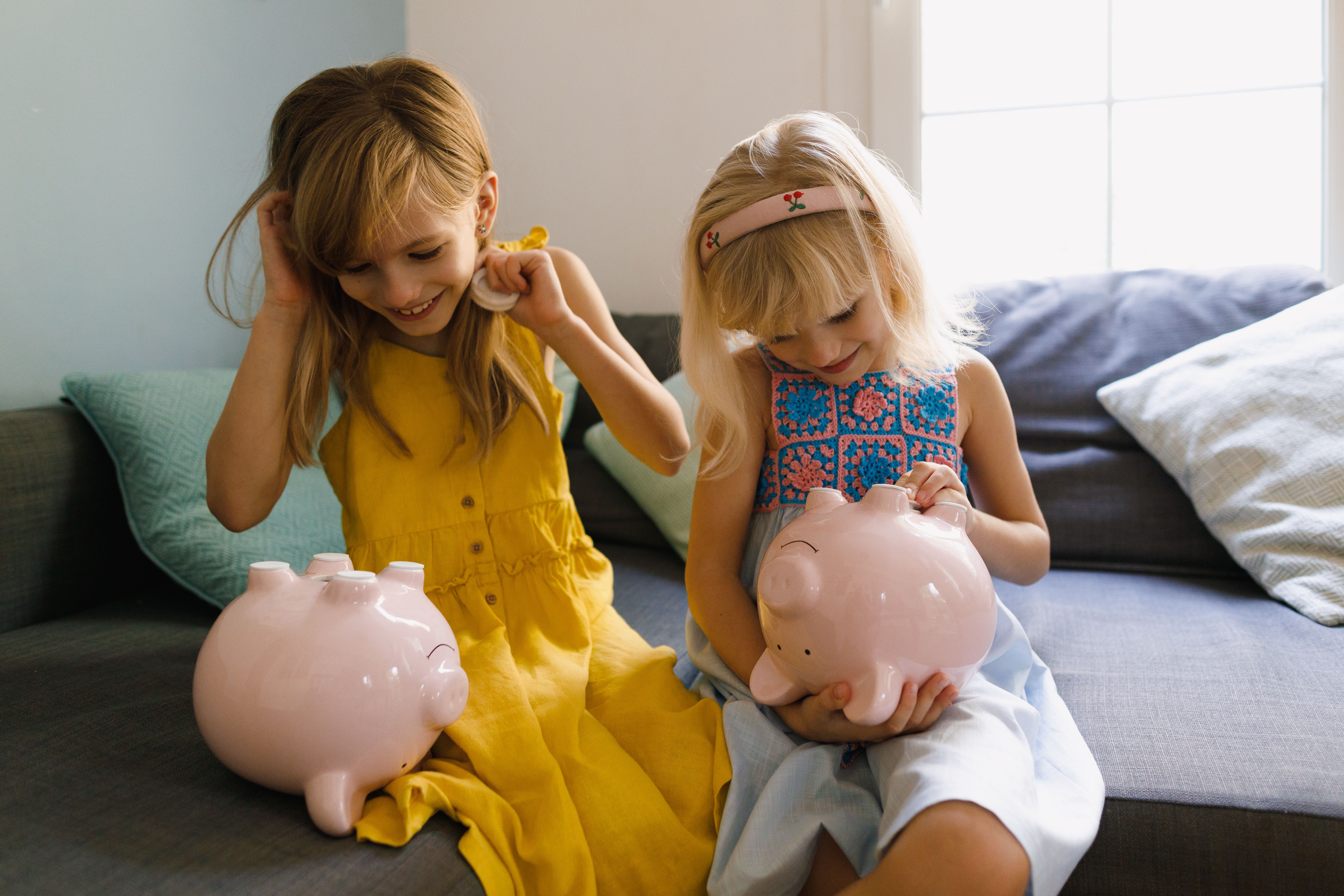 Two young girls putting money into their pink piggy banks