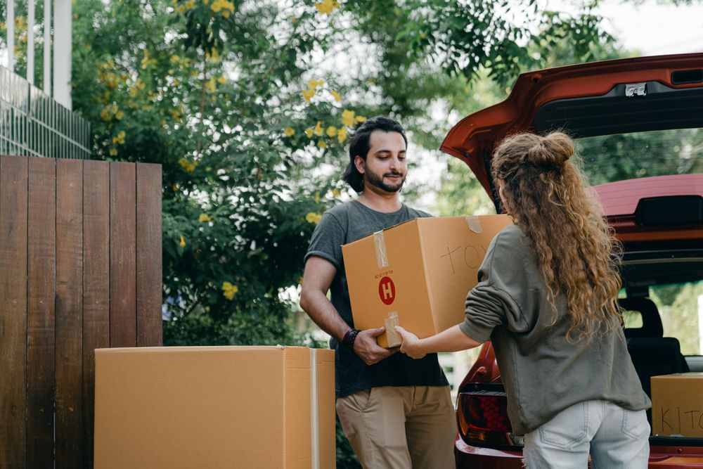 couple moving brown boxes into red car boot