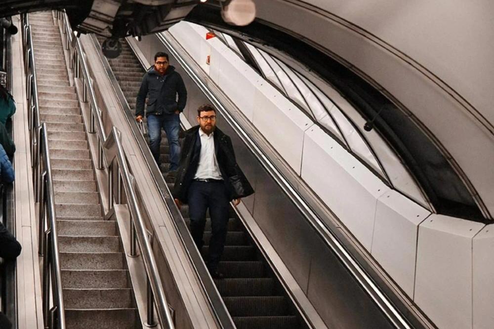 Two people travel downwards on an escalator. They look determined.