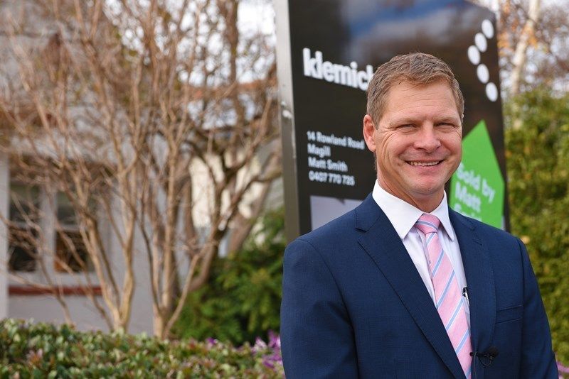 Matt Smith stands in front of klemich real estate sign and house for sale 