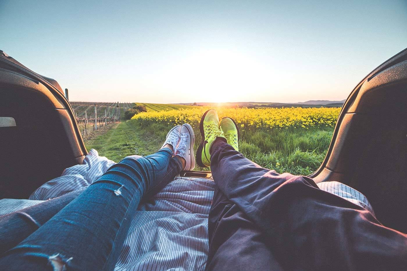 Two people wearing jeans and sneakers lying in back of a car overlooking a field of flowers