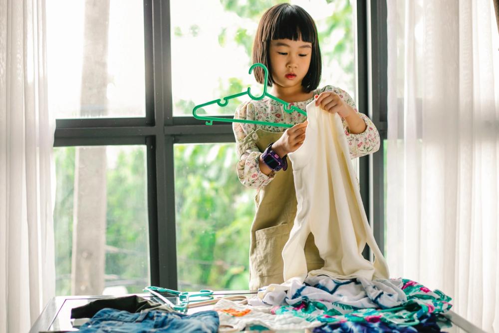 Young girl putting clothes on a hanger