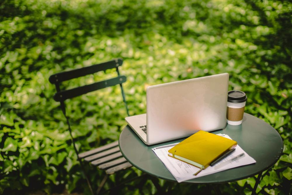 Table and chair set up in garden. Laptop and notebook on table.