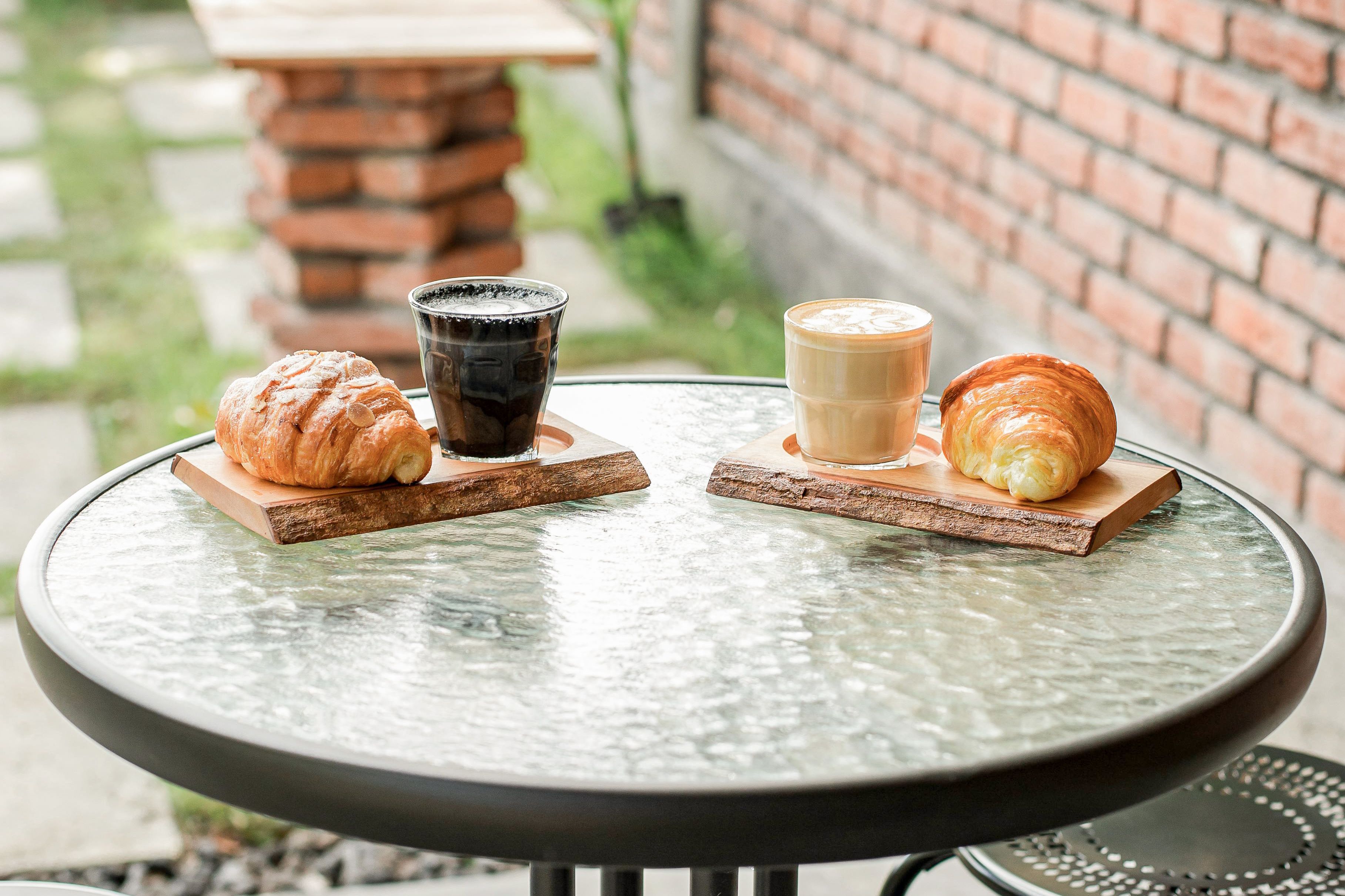 An outdoor table setting for two. Two pairs of coffee and croissants are set up.