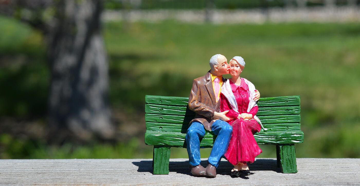 Figurine of old couple sitting on bench kissing 