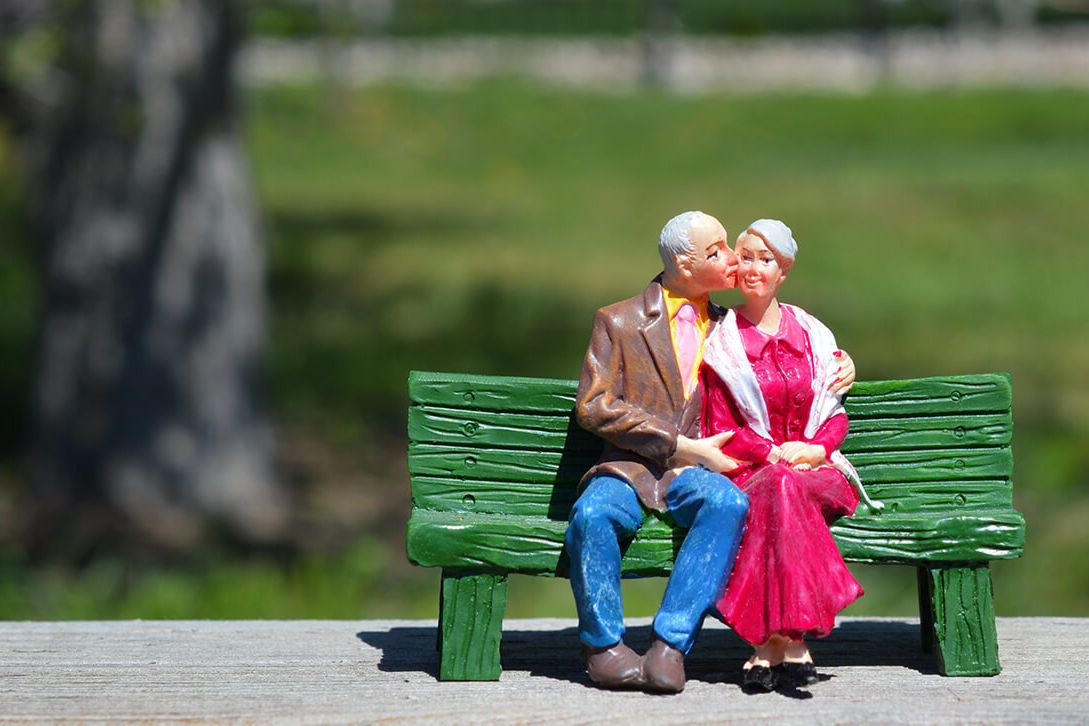 Figurine of old couple sitting on bench kissing 