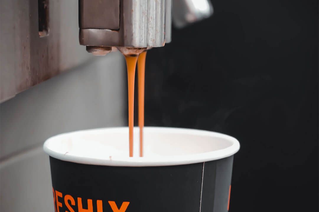 Coffee pouring from a coffee machine into a disposable cup.