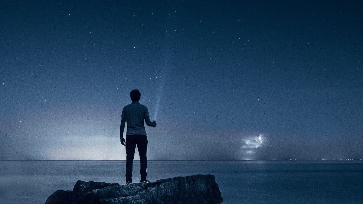 Person standing on rock over ocean with torch at night