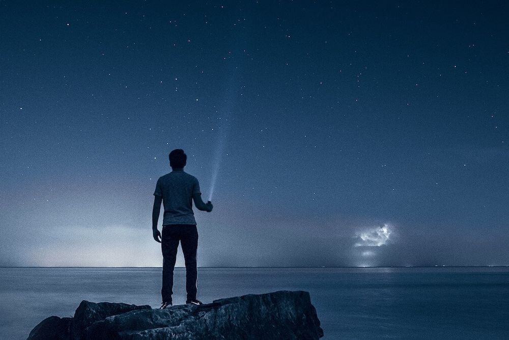 Person standing on rock over ocean with torch at night