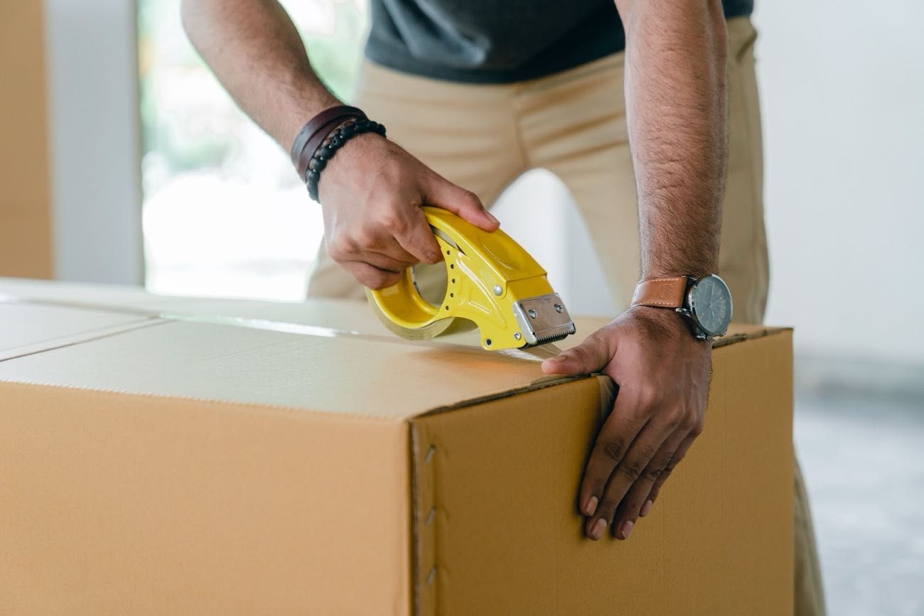 Cropped man sealing a packing box. Arms and legs close up visible only.