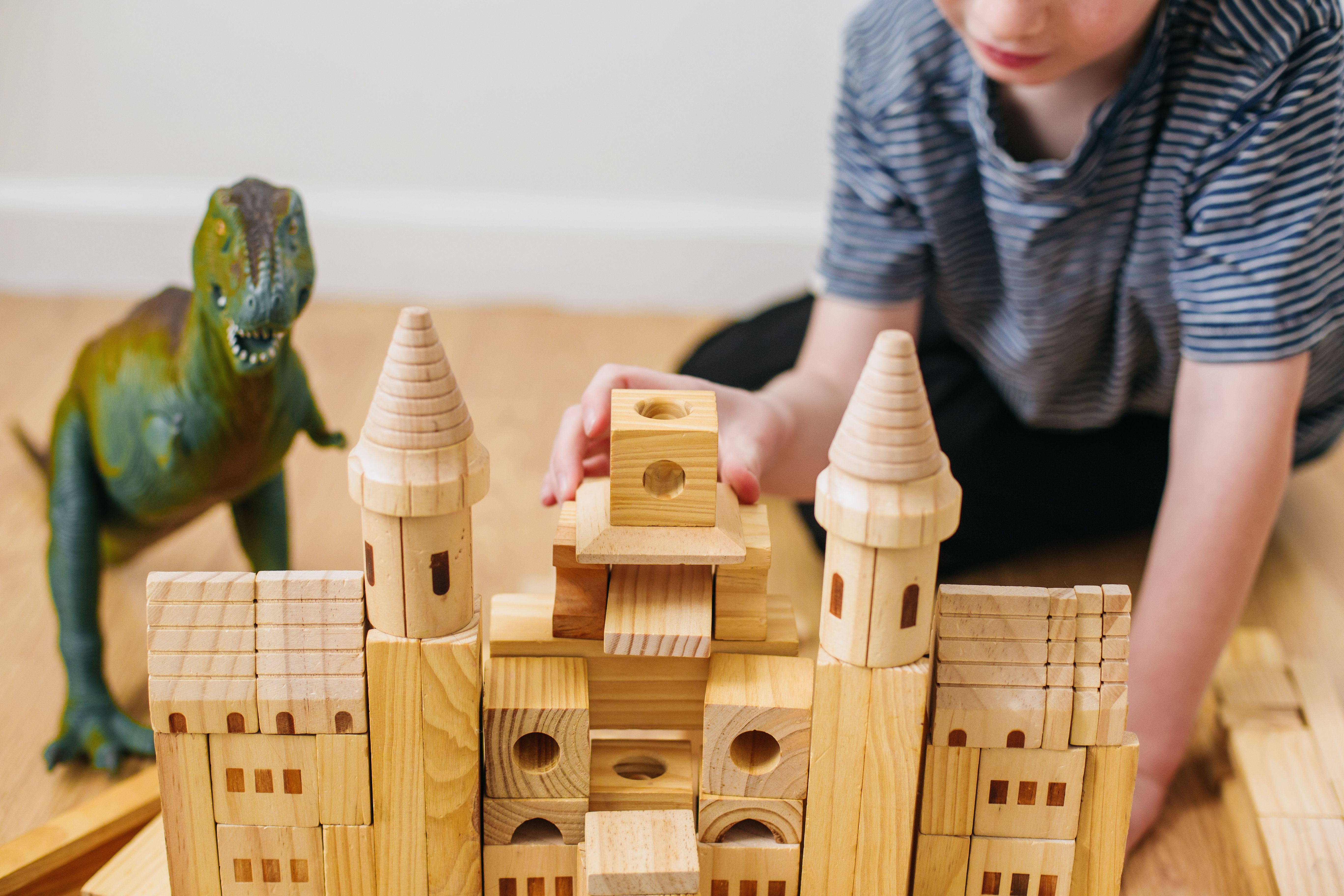 Young boy building wooden castle with his toy dinosaur 