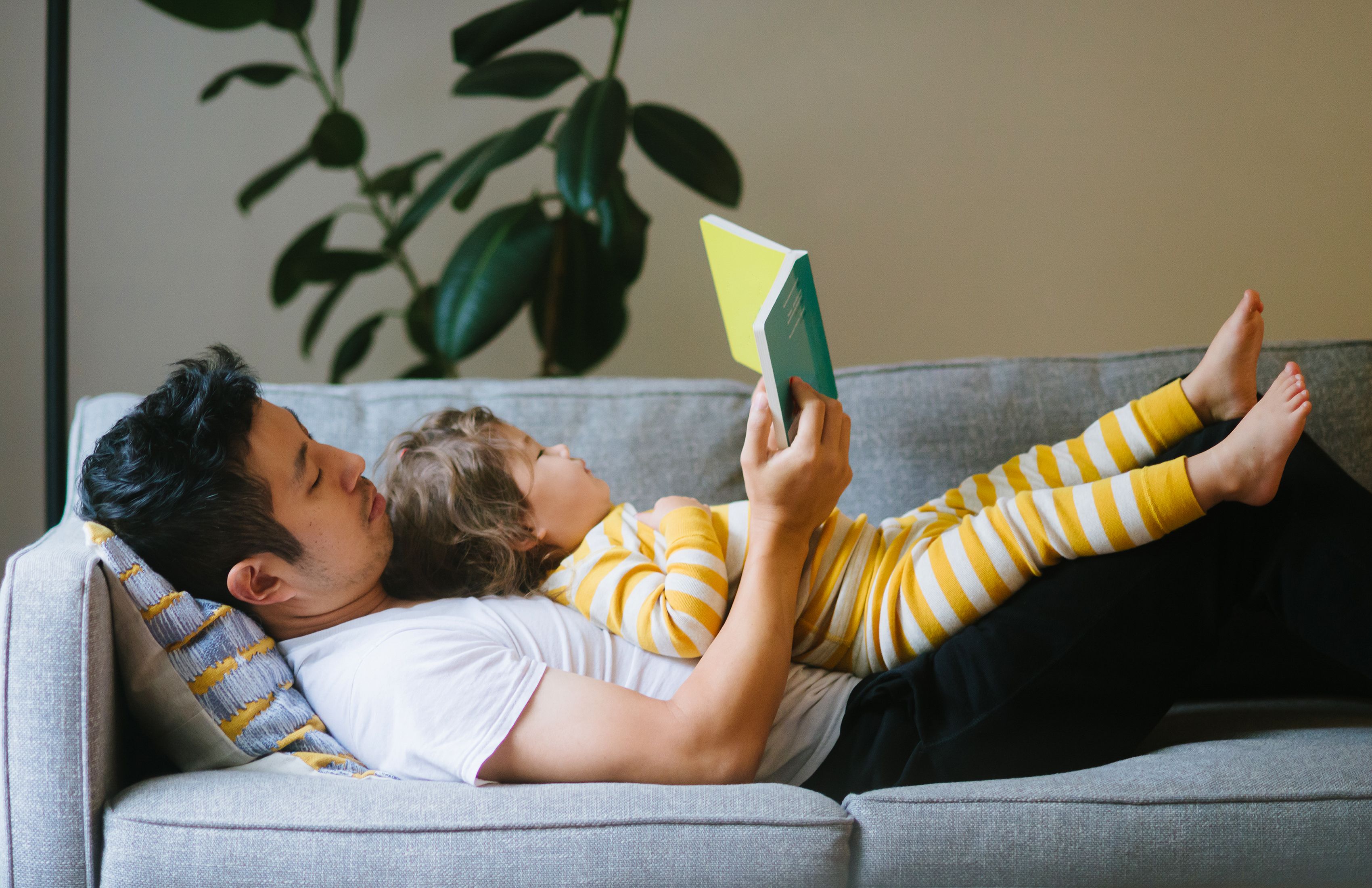 Father reading to daughter lying on his chest on the couch 