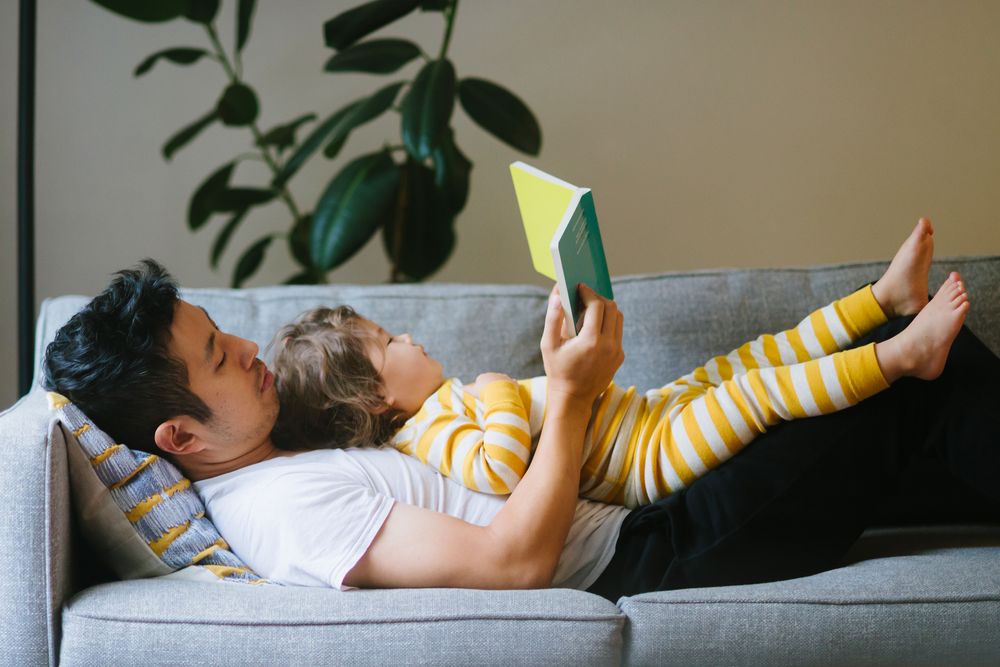 Father reading to daughter lying on his chest on the couch