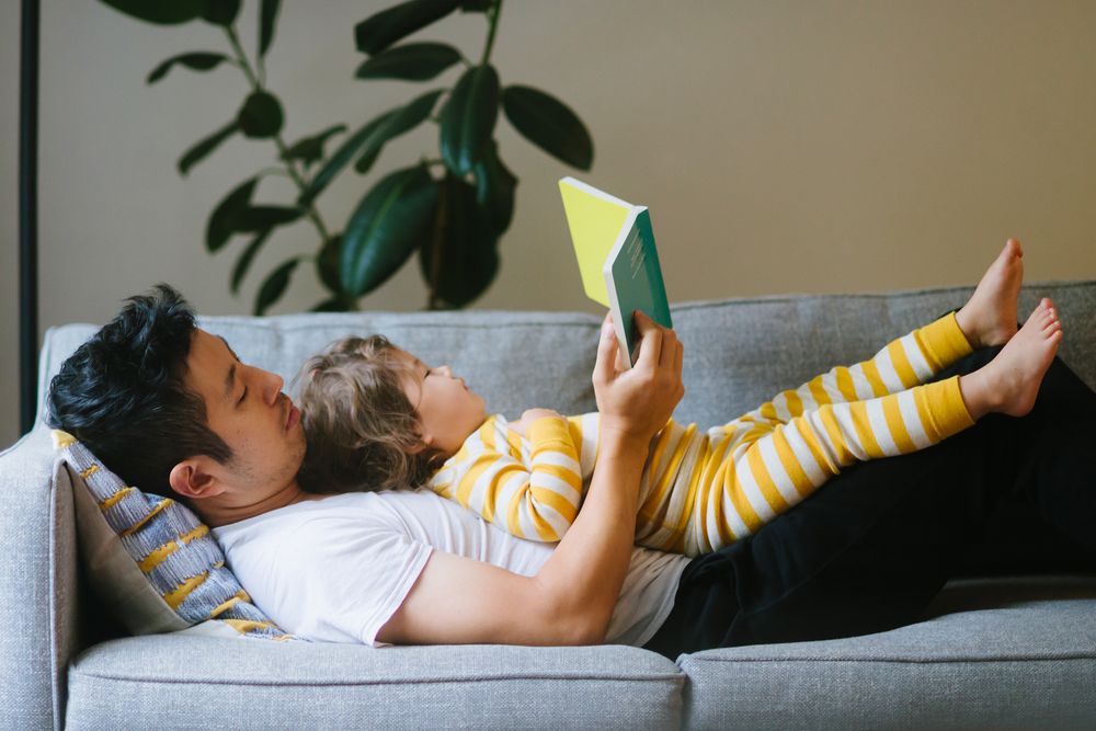Father reading to daughter lying on his chest on the couch 