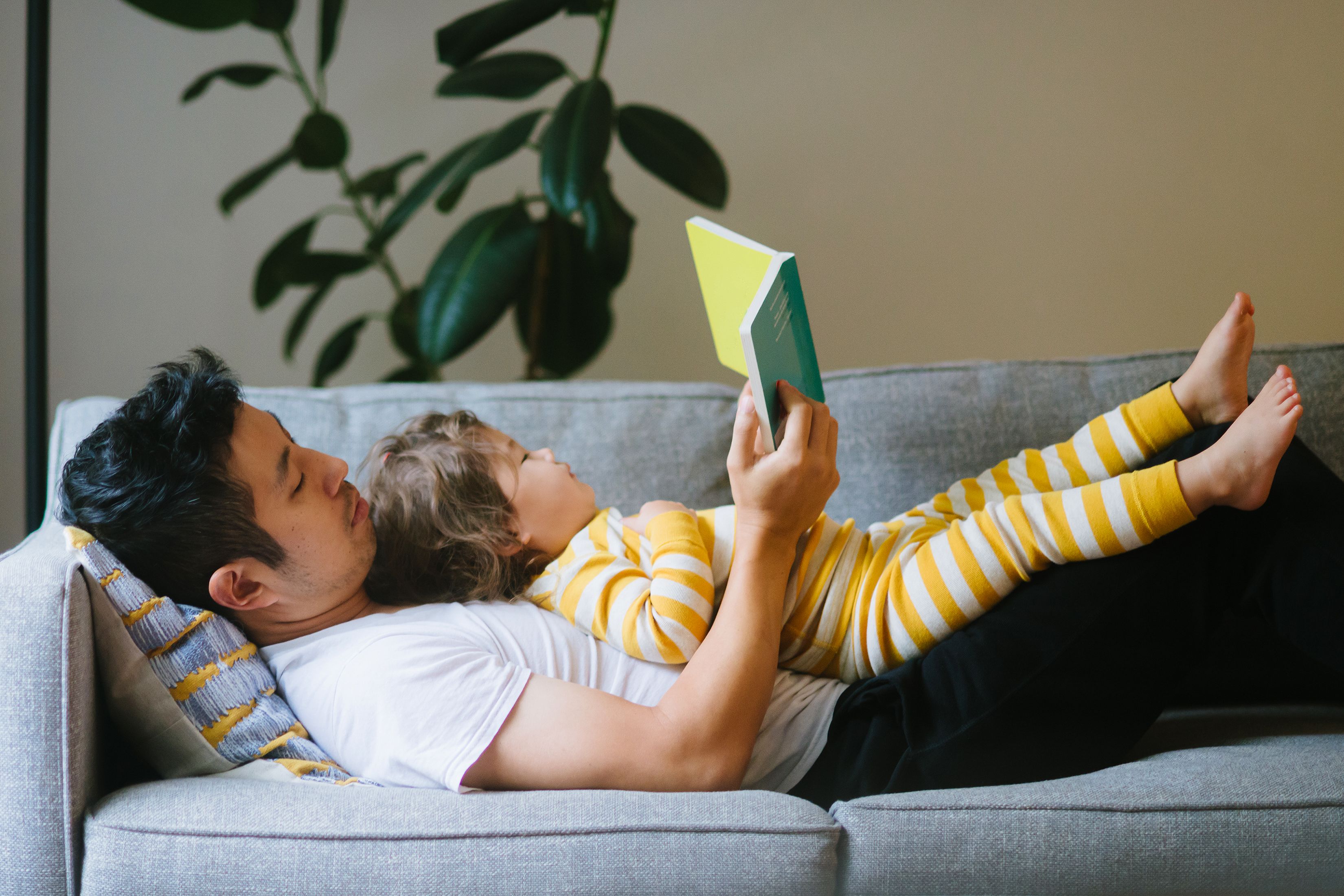 Father reading to daughter lying on his chest on the couch