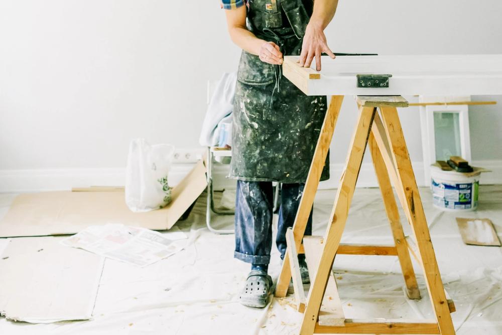 Person standing at a construction table in a room in the middle of a renovation. Person is in paint-splattered work clothes.