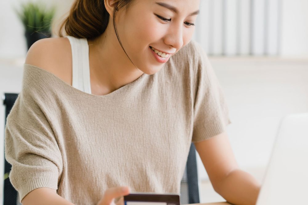 Person sitting at a laptop, with credit card in hand. They are smiling, which suggests they are making an online purchase.