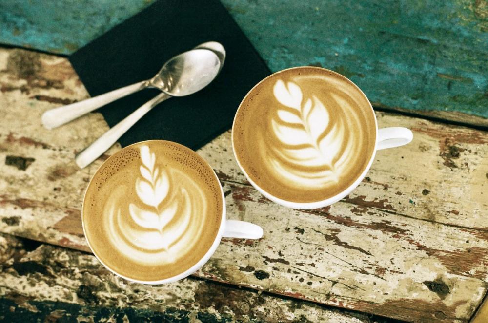 Overhead image of two identical coffees on a bench with two spoons on a napkin