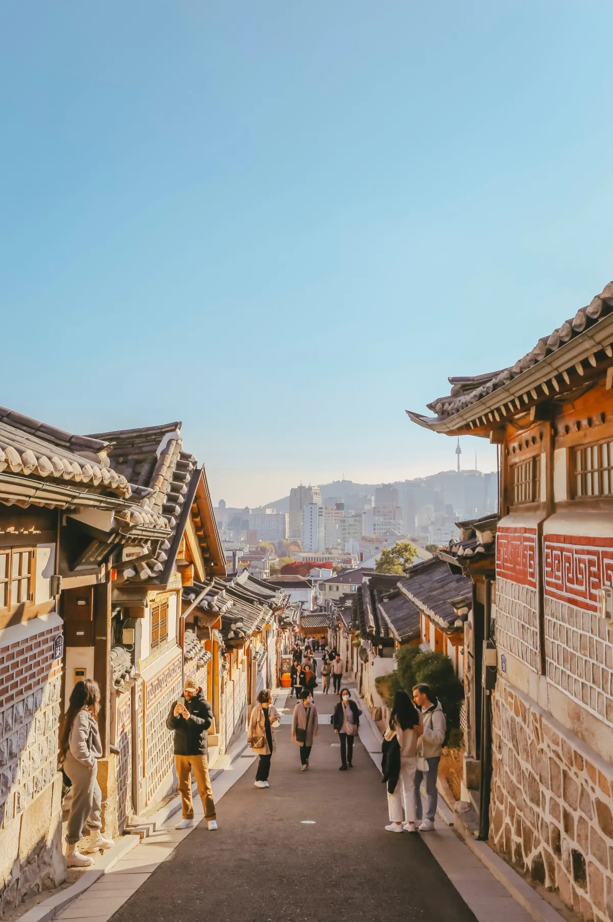 기와 지붕 사이로 비탈진 북촌한옥마을 골목을 거니는 방문객들과 멀리 보이는 남산타워