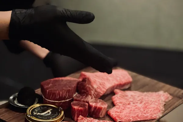 A chef presents a wooden board of marbled Hanwoo cuts — tenderloin, striploin and thin-sliced cuts — with black truffle and caviar at KUT SEOUL