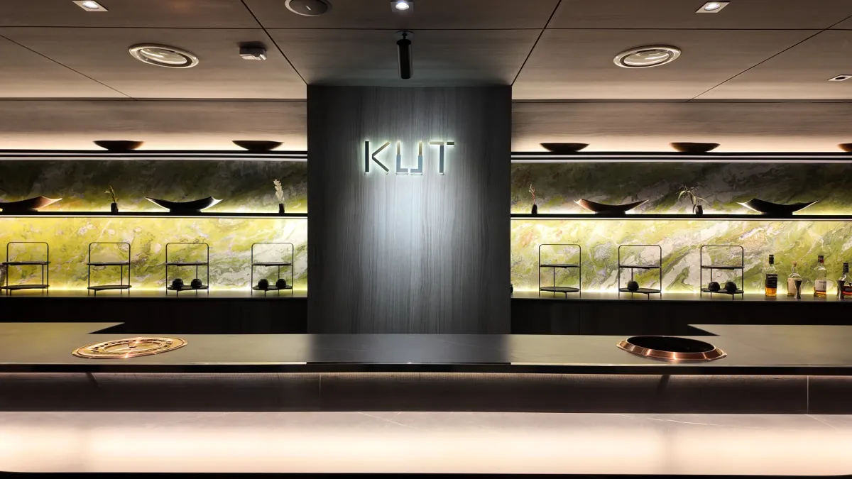 KUT SEOUL omakase counter with backlit jade stone wall, dark oak signage, and copper grill inlays