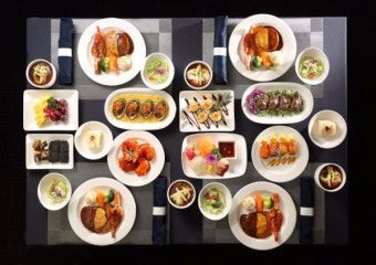 Overhead view of a curated Korean course meal with Hanwoo, sashimi, tempura, and banchan on a dark linen table