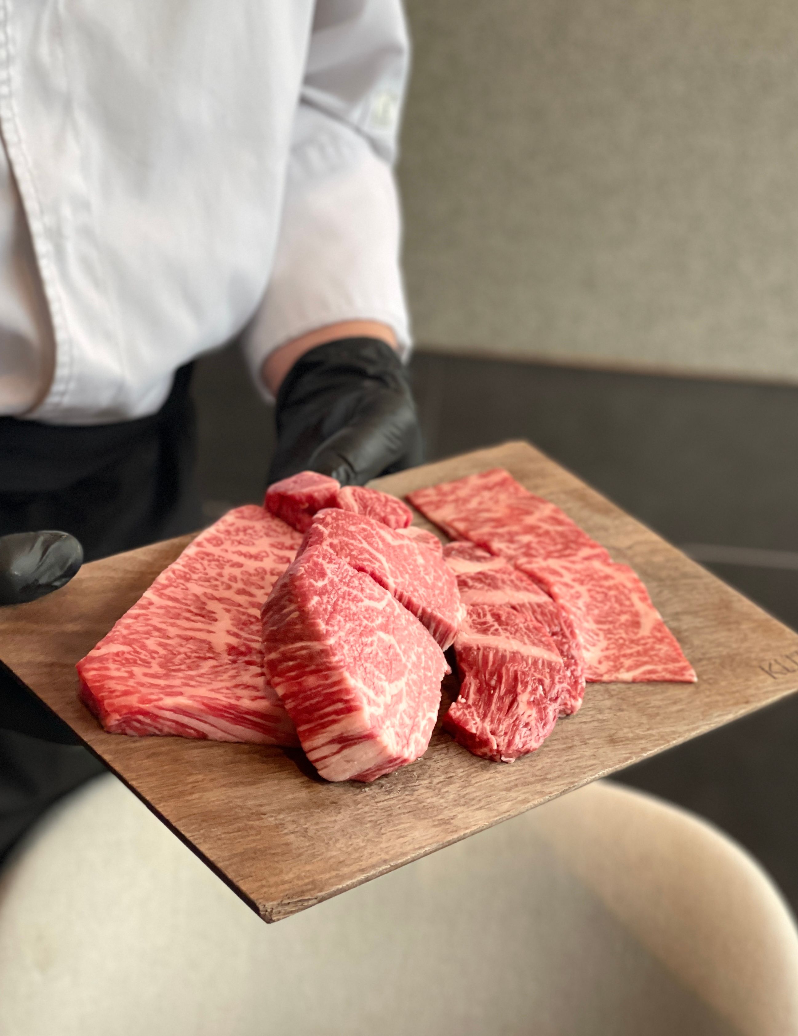 Chef in white jacket presents a wooden board of marbled Hanwoo beef cuts showcasing BMS no.9 grade