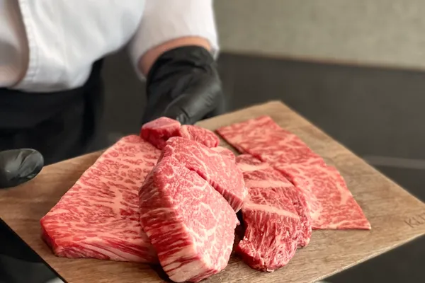 Chef in white jacket presents a wooden board of marbled Hanwoo beef cuts showcasing BMS no.9 grade